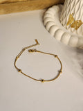 Gold snake chain ball station bracelet laid flat on white surface