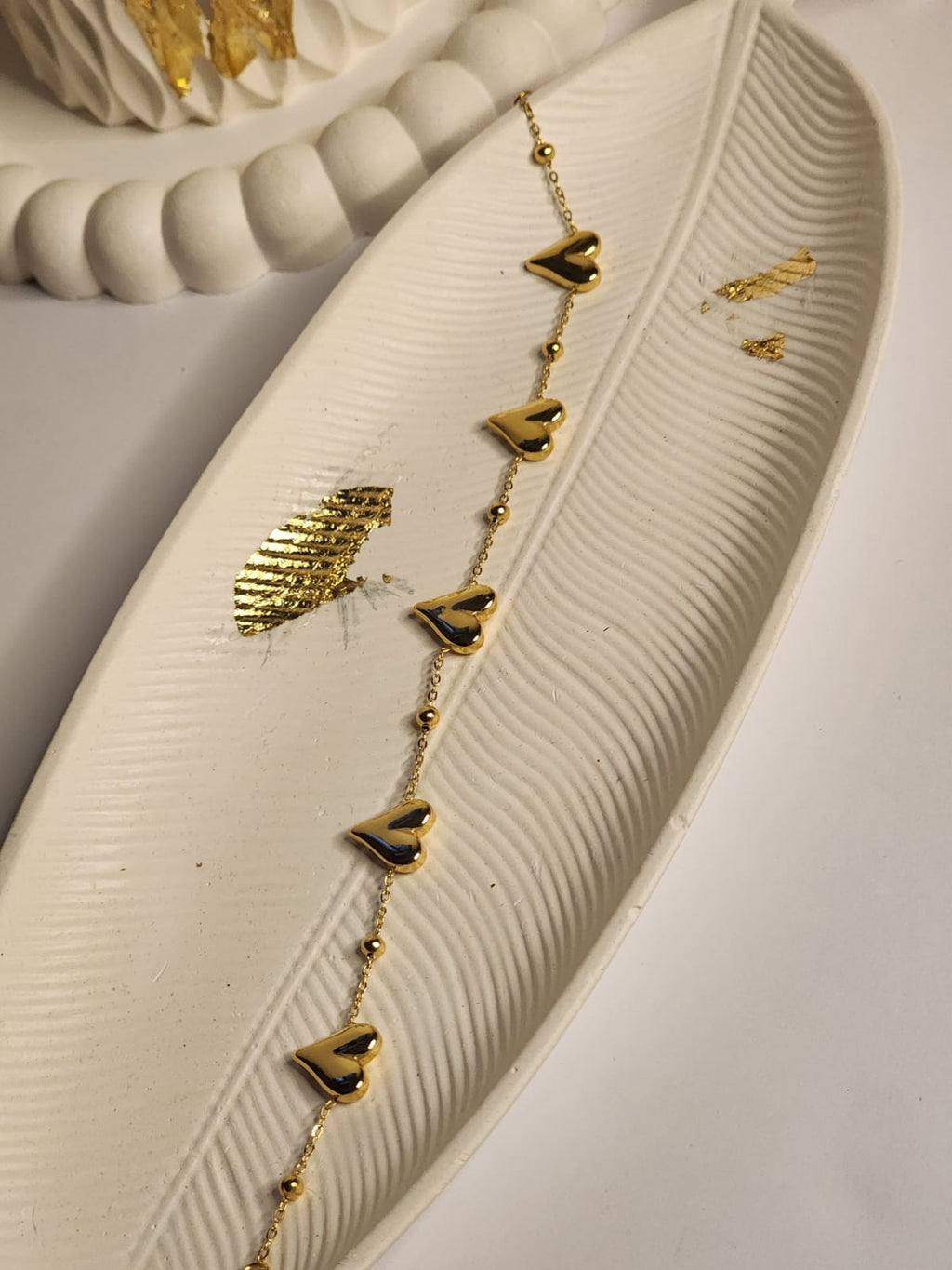 Multi heart gold chain bracelet laid flat on white feather tray