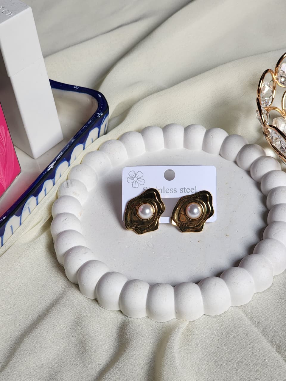 Gold wavy abstract pearl stud earrings front view on white display tray