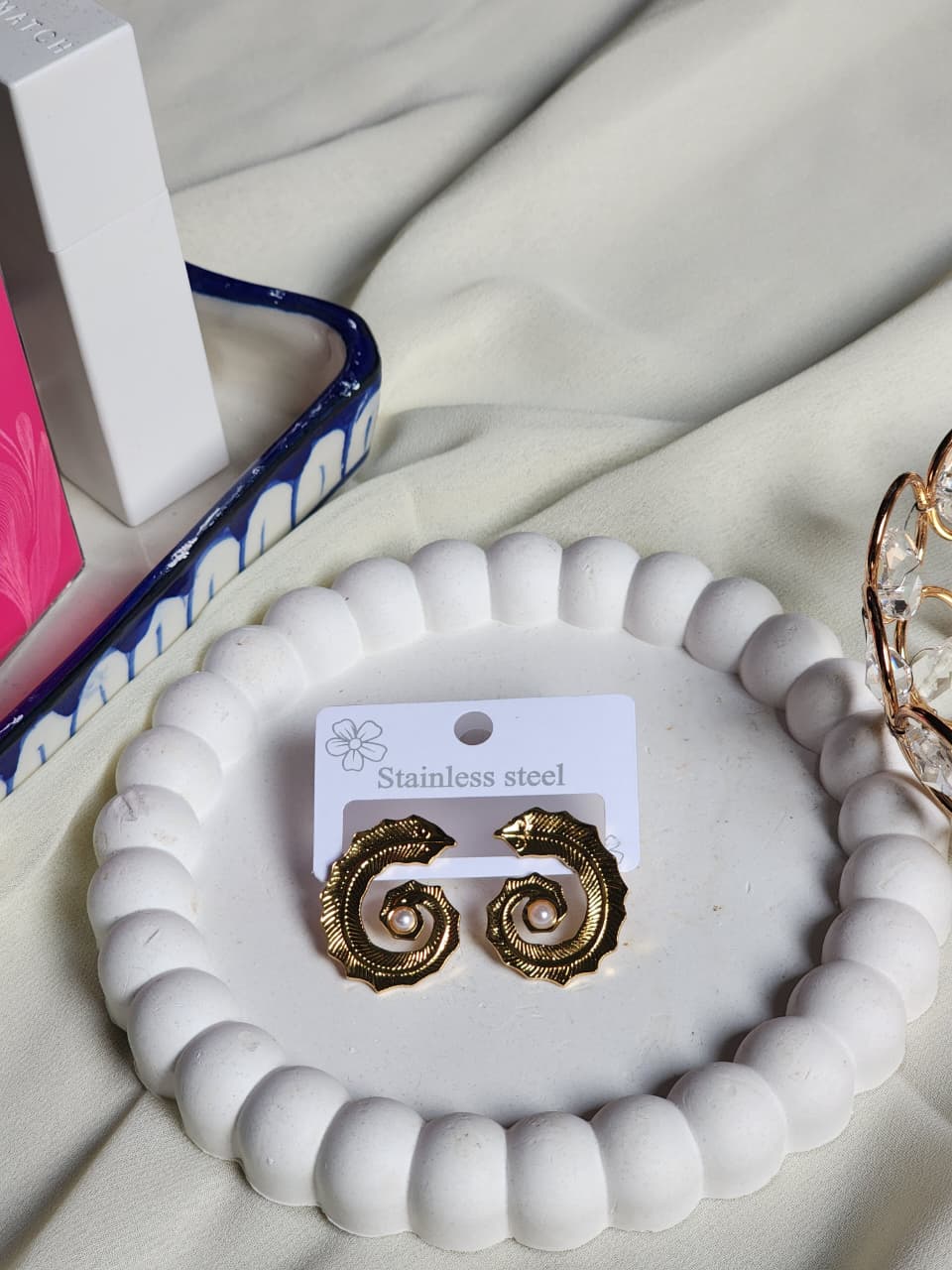 Gold spiral swirl stud earrings with pearl centre on white display tray