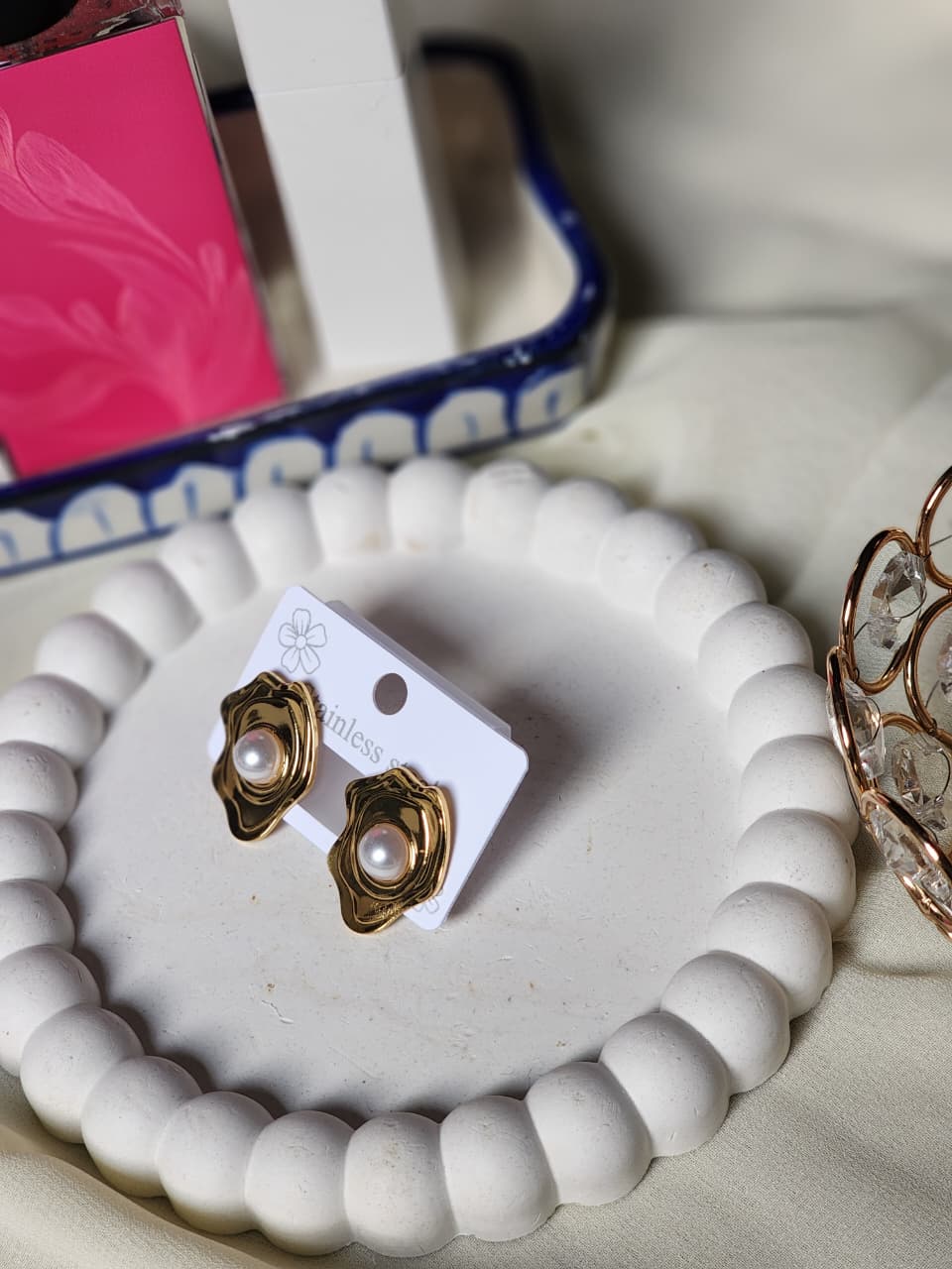 Gold wavy abstract stud earrings with pearl centre on white display tray