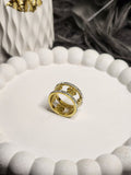 Wide gold floral cutwork ring with crystal edges on white display stand