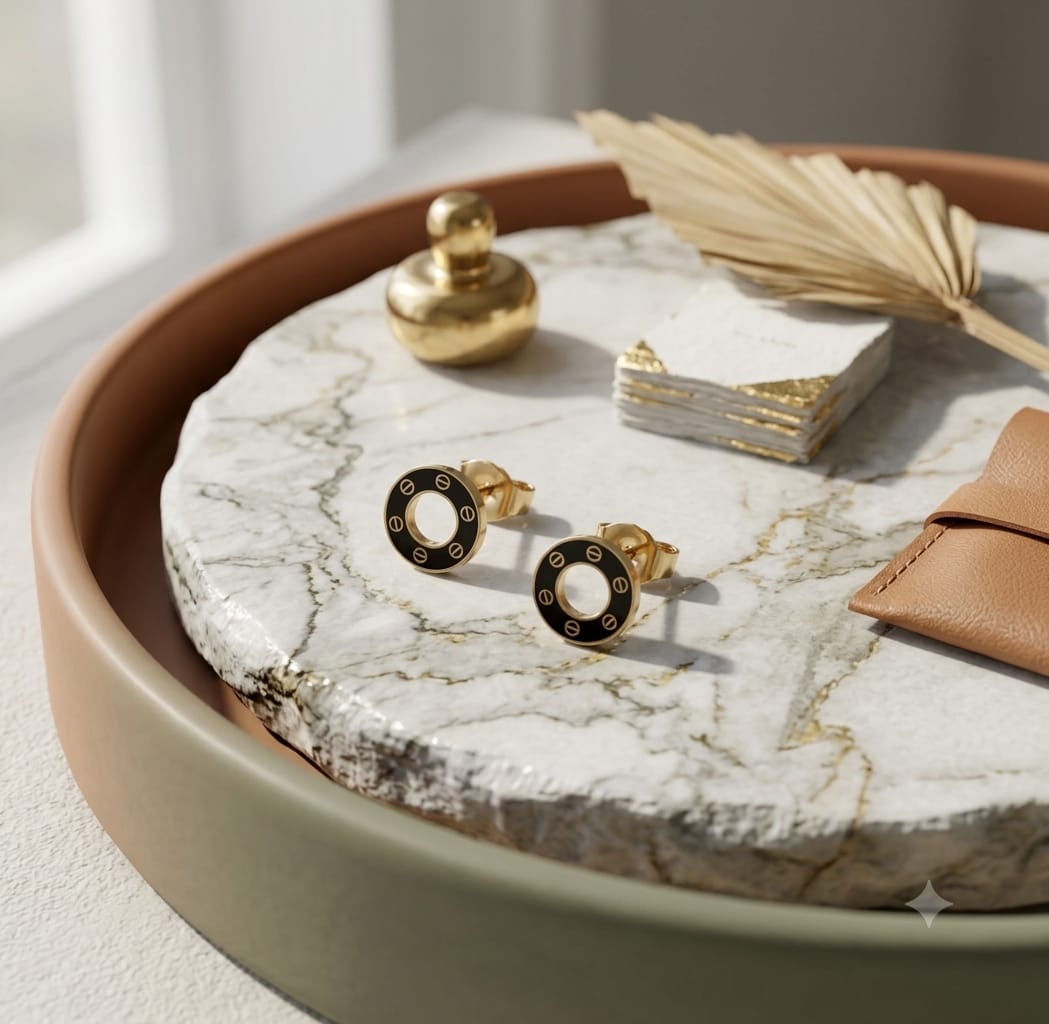 Black enamel open circle stud earrings with gold-tone screw-detail border on marble surface