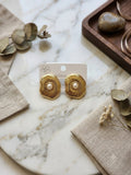 Gold textured flower stud earrings with pearl centre on marble surface
