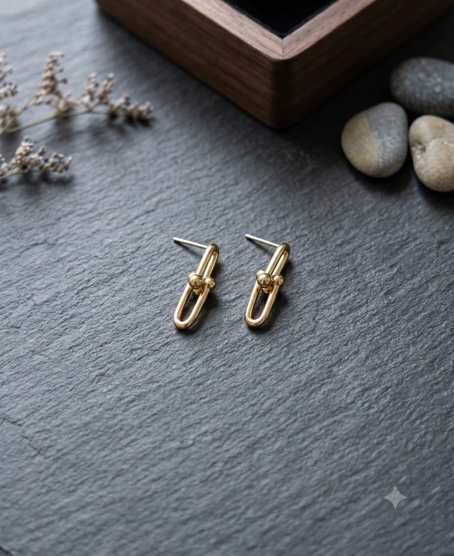 Gold oval link drop stud earrings with ball connector on slate surface