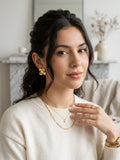 Gold textured flower drop earrings worn on model with layered necklaces