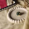 A high-angle shot of a bold dome-shaped statement ring featuring a deep emerald green malachite texture with swirling polished gold inlays, displayed on a white beaded decorative tray.