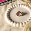 A close-up shot of a single-bloom statement ring featuring lilac, set on a premium gold finish base and displayed on a white decorative tray.