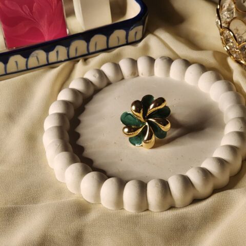 A sculptural gold statement ring featuring a pinwheel design with alternating deep emerald green enamel and polished gold petals.