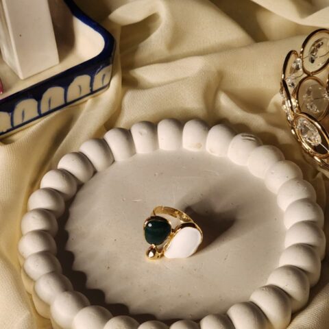 A modern gold statement ring featuring two smooth, organic pebble-shaped stones in deep forest green and crisp white, accented by a small gold bead.