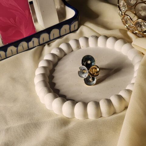 A contemporary gold-tone ring featuring a cluster of four cupped, flower-like petals in shades of slate grey, light blue-grey, and polished gold.