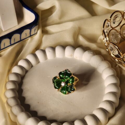 Close-up photo of a gold-finish statement ring featuring handcrafted deep emerald green petals with shimmering crystal centers.