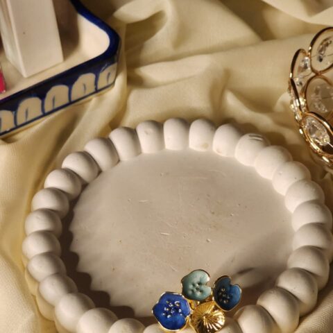 A close-up shot of a multi-bloom statement ring featuring three distinct floral forms in cobalt blue, teal blue, and gold finishes, displayed on a white decorative tray.